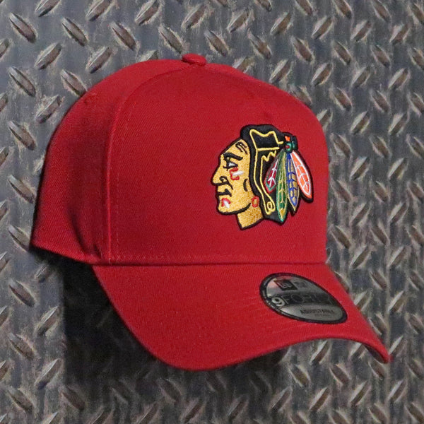 A red baseball cap featuring the embroidered Chicago Blackhawks logo on the front, displayed against a textured gray diamond plate background. New Era Chicago Blackhawks 9FORTY A-Frame Snapback Hat RED 60646501