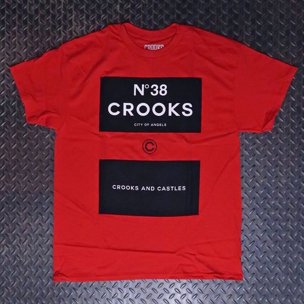 A red short-sleeve t-shirt with two black rectangular graphic panels on the front, laid flat on a dark textured diamond plate background. The top panel reads 'N°38 CROOKS' and the bottom panel reads 'CROOKS AND CASTLES'. Crooks & Castles Klepto T-Sirt Red 5Z57051
