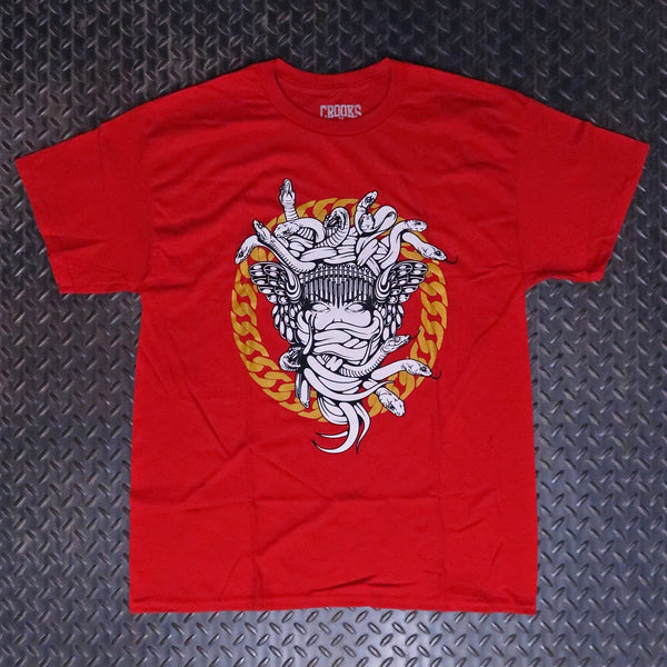 A red short-sleeve graphic t-shirt laid flat on a dark textured diamond plate background. The shirt features a large central graphic of a white skeletal figure with wings and multiple snake heads, set against a circular gold and red chain design. Crooks & Castles Cuban Link T-Shirt Red 5Z57043D