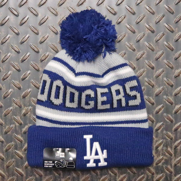 A blue and white knit beanie with a pom-pom, featuring the word 'DODGERS' across the front and an 'LA' logo on the cuff. A New Era 9FIFTY brand tag is attached to the cuff. New Era Los Angeles Dodgers Knit Pom Beanie Blue Grey White 60399779