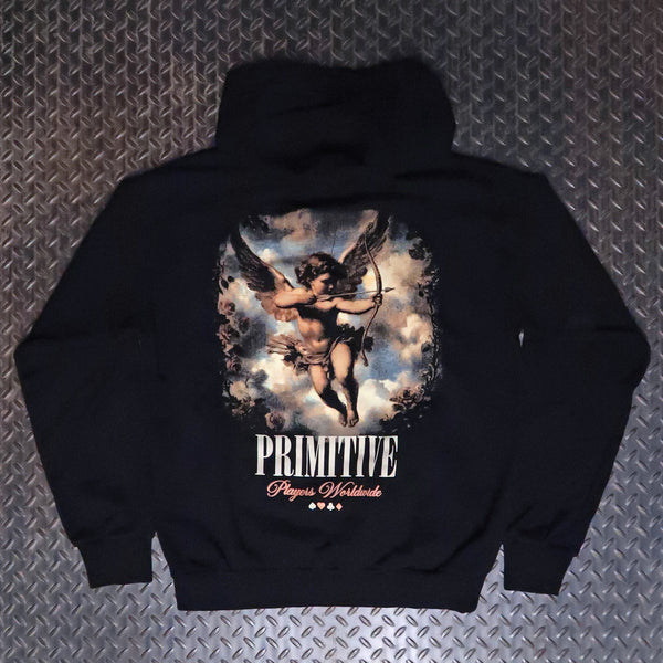A black hooded sweatshirt laid flat on a textured gray diamond plate background. The back of the hoodie features a large graphic print of a winged cupid holding a bow, with the text 'PRIMITIVE' and 'Players Worldwide' printed below. Primitive Players Pullover Hoodie Black PAPFA2556